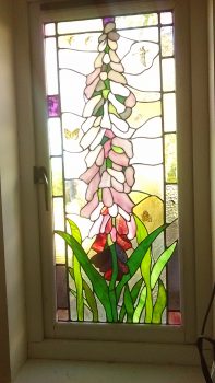 flower window showing,one foxglove varying in colou from white to pale pink, dark pink purple and violet. Painted on are a goose, heron, oystercatcher